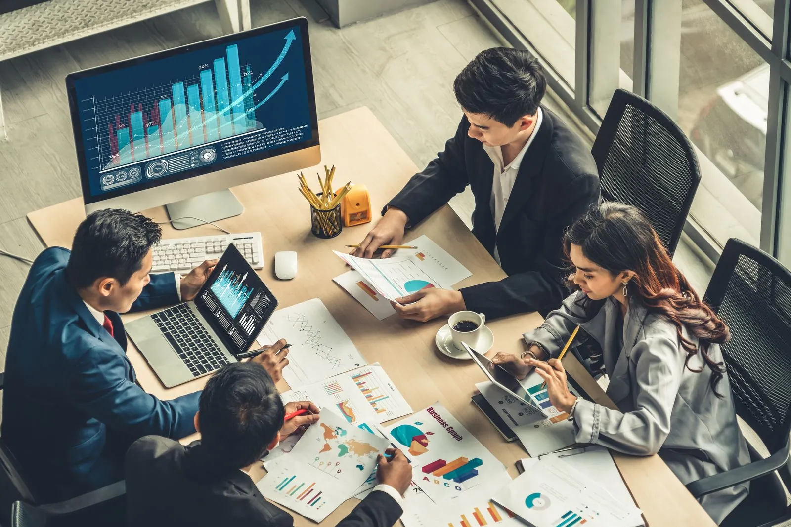 A commercial team clustered around a desk of monitors showing sales charts and performance dashboards.