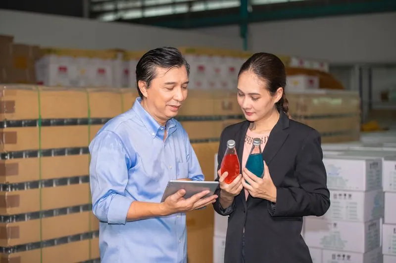 Two colleagues checking beverage stock against a tablet in a warehouse.