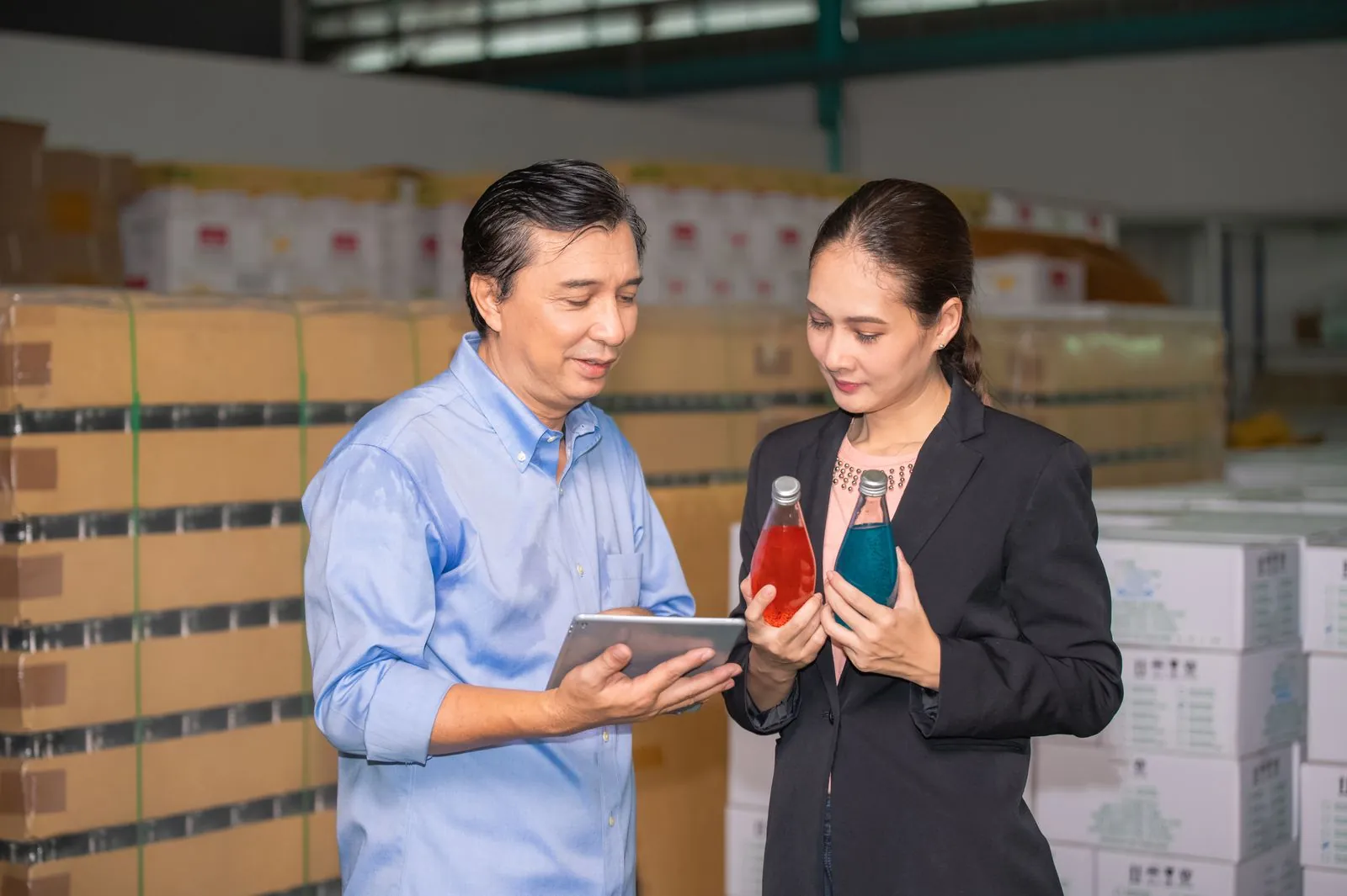A distributor sales manager and a supplier representative reviewing product cases on a tablet in a beverage warehouse.