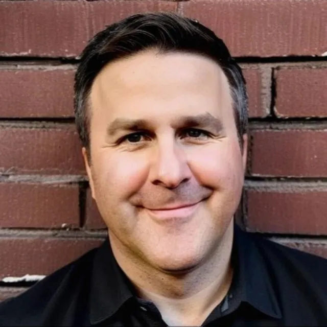 Portrait of Randy Browne, advisor to BevGenie, wearing a dark shirt in front of a brick wall.